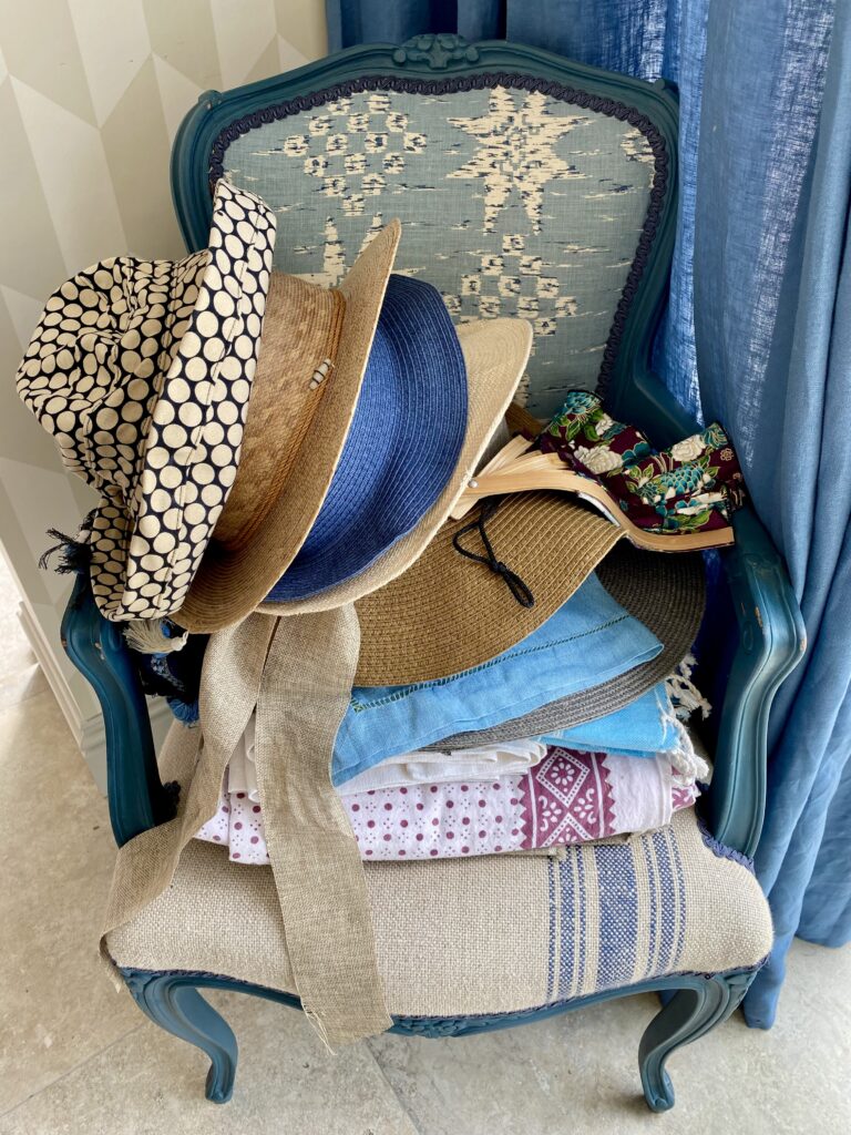 A French style carver chair with a pile of summer hats and table linen.