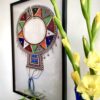 A framed Maasai beadwork collar necklace with yellow gladioli in a vase in the foreground.