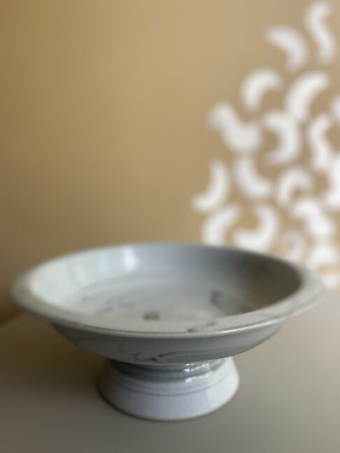 Rustic Thai pottery in off-white in front of a warm beige backdrop.