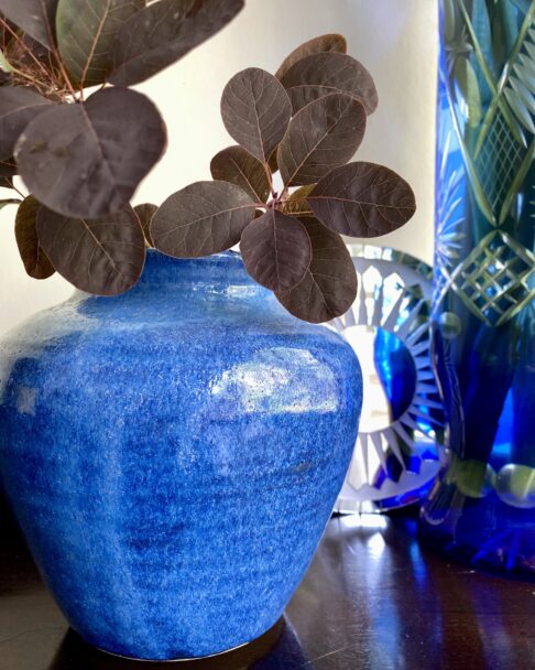 A vivid blue ceramic pot with a tall, blue cut glass vase in the background.