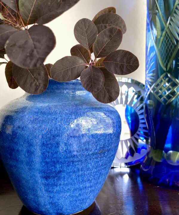 A vivid blue ceramic pot with a tall, blue cut glass vase in the background.