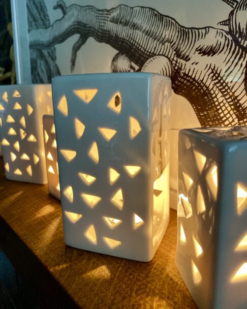 Illuminated, pierced tea light holders glowing on a shelf.