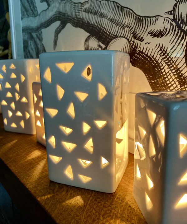 Illuminated, pierced tea light holders glowing on a shelf.