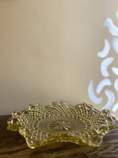 A vintage, gold-coloured, pressed glass plate with scalloped, wavy edges.