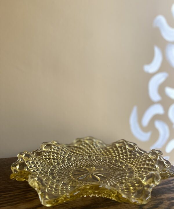 A vintage, gold-coloured, pressed glass plate with scalloped, wavy edges.