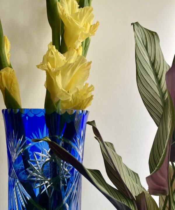 Detail of the rim if a tall, Royal blue, cut glass vase filled with yellow Gladioli.