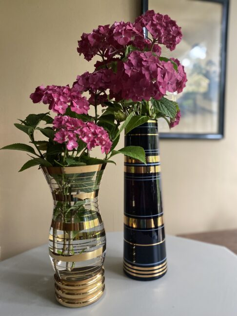 Two retro, striped, glass vases with gold-coloured detailing and filled with pink hydrangeas.