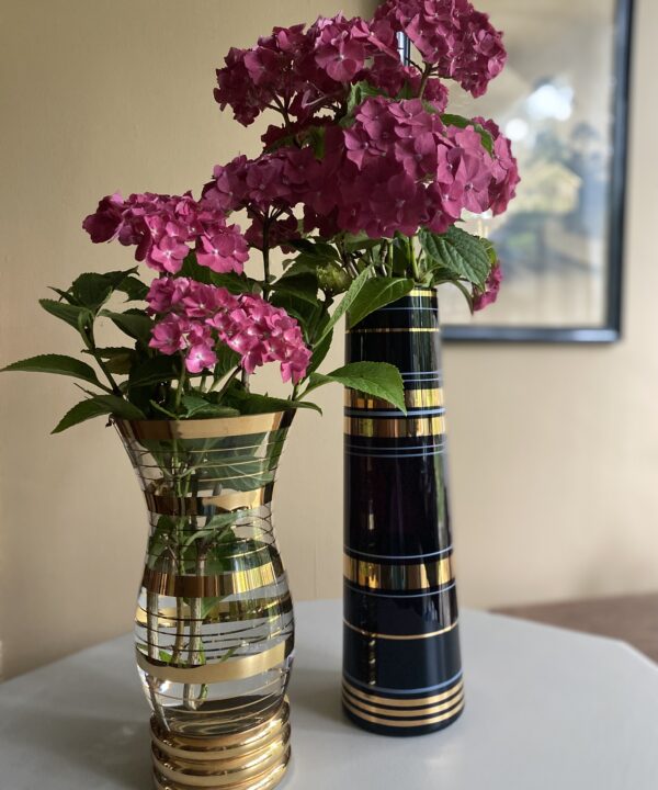 Two retro, striped, glass vases with gold-coloured detailing and filled with pink hydrangeas.