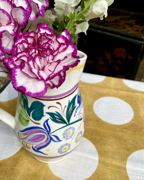 A pretty, multi-coloured Poole pottery jug used as a vase for blooms.