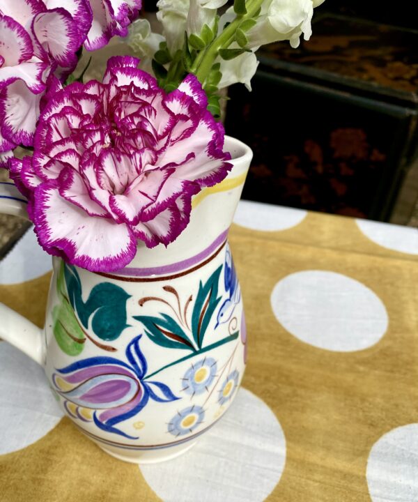 A pretty, multi-coloured Poole pottery jug used as a vase for blooms.