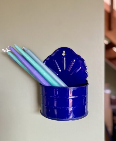 A scalloped, wall-mounted, vintage salt box in blue enamel holding candles from H&M Home.