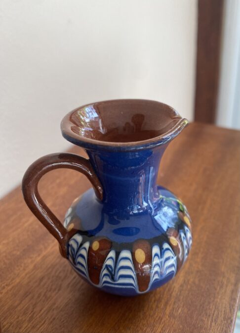 Bulgarian Troyan pottery in miniature on a wooden shelf.