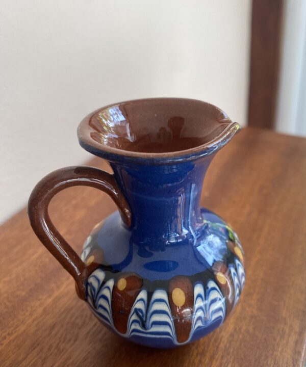 Bulgarian Troyan pottery in miniature on a wooden shelf.