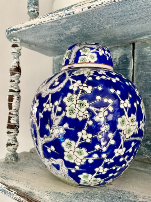 A vibrant Royal blue and soft green lidded ginger jar with blossom decoration, shown here on vintage blue shelving.