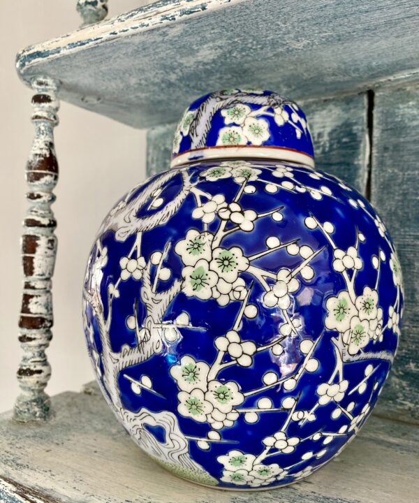 A vibrant Royal blue and soft green lidded ginger jar with blossom decoration, shown here on vintage blue shelving.