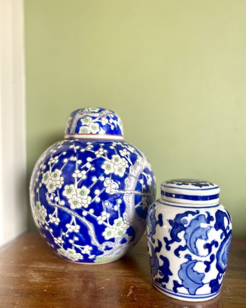 Vintage lidded pots in different sizes against a green wall.