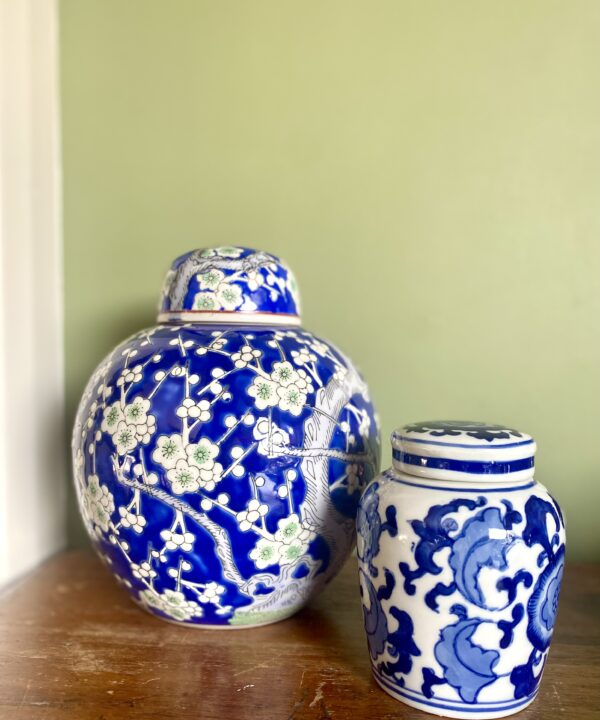 Vintage lidded pots in different sizes against a green wall.