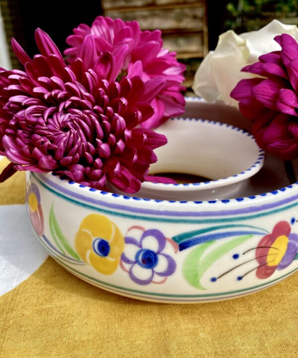 A colourful Poole pottery posy ring filled with pink blooms.