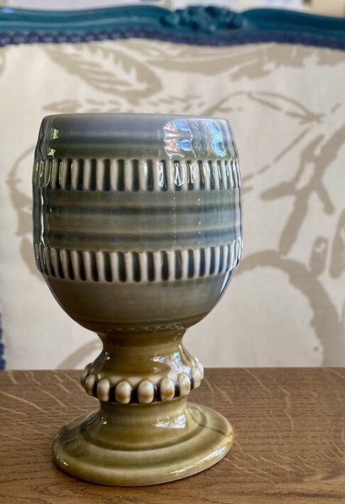 A hand-decorated, vintage, Irish pottery goblet or bud vase by Wade on a wooden tabletop.