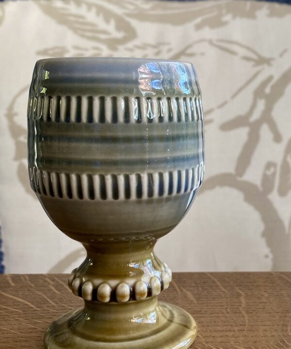 A hand-decorated, vintage, Irish pottery goblet or bud vase by Wade on a wooden tabletop.