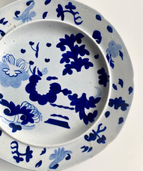 An antique blue and white plate for wall decoration, with Chinese-inspired, hand-painted detailing.