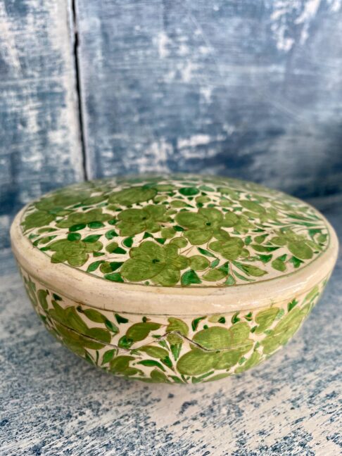 An Indian papier mâché pot in cream and lime green sat on vintage blue shelves.