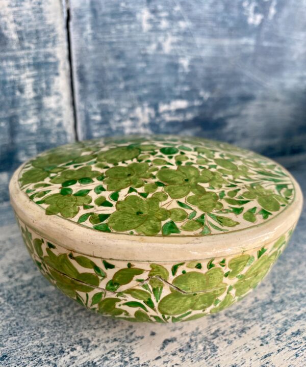 An Indian papier mâché pot in cream and lime green sat on vintage blue shelves.