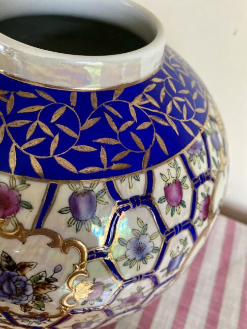 The neck and rim of a vintage Chinese globe vase with florals in pink and blue and gilt detailing.