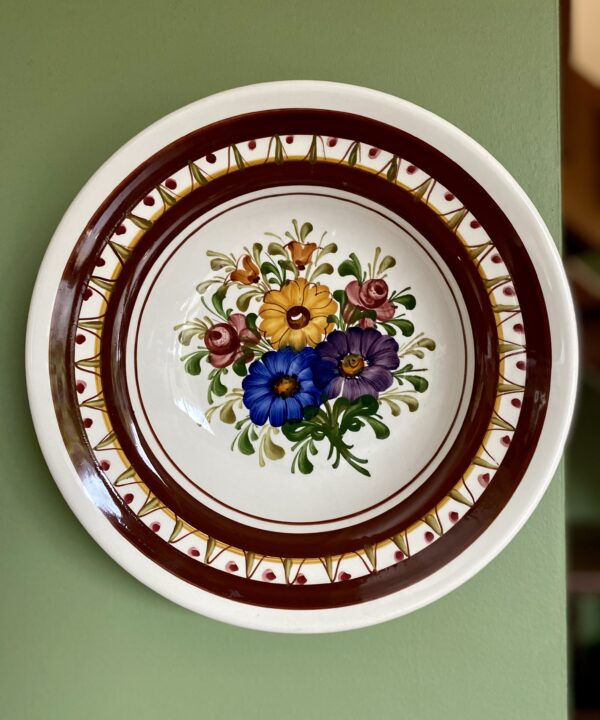 A decorative, hand-painted, vintage wall plate from Austria against a green wall.