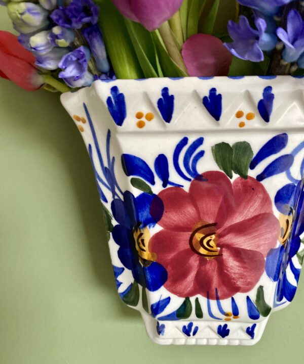 A vase on the wall with hand-painted florals and real flowers.