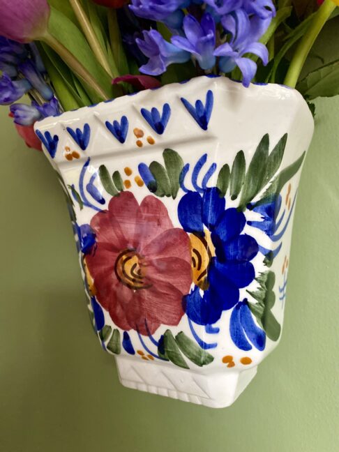 Hand-painted decoration in Royal blue, deep pink and olive green depicting flowers and foliage on a wall vase.