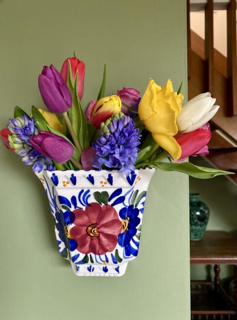 A hand-painted vintage wall vase with floral decoration, itself filled with Spring blooms.