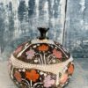 A vintage Indian papier mâché trinket pot with domed lid in pink, orange and lilac with gold detailing.