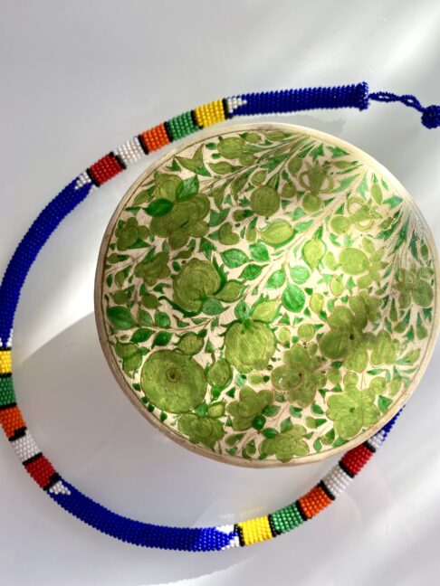 Papier mâché trinket pot in green shown on a glass surface with an African beaded necklace.