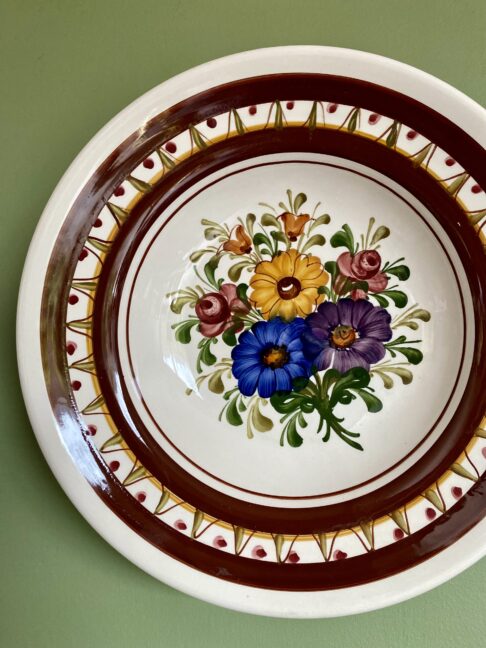 A floral bouquet hand-painted on a wall plate hung on a green wall.