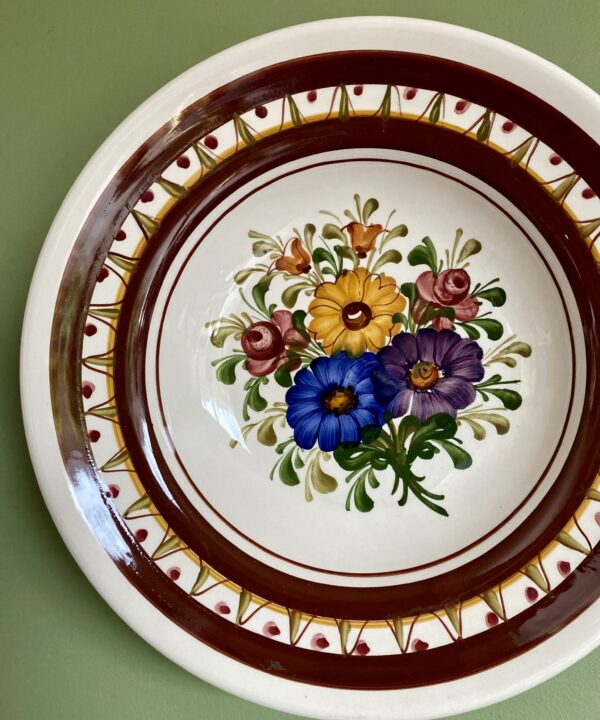 A floral bouquet hand-painted on a wall plate hung on a green wall.