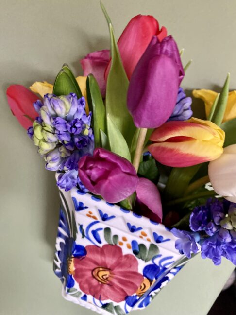 A vintage, wall-mounted vase filled with pretty tulips, hyacinths and roses.