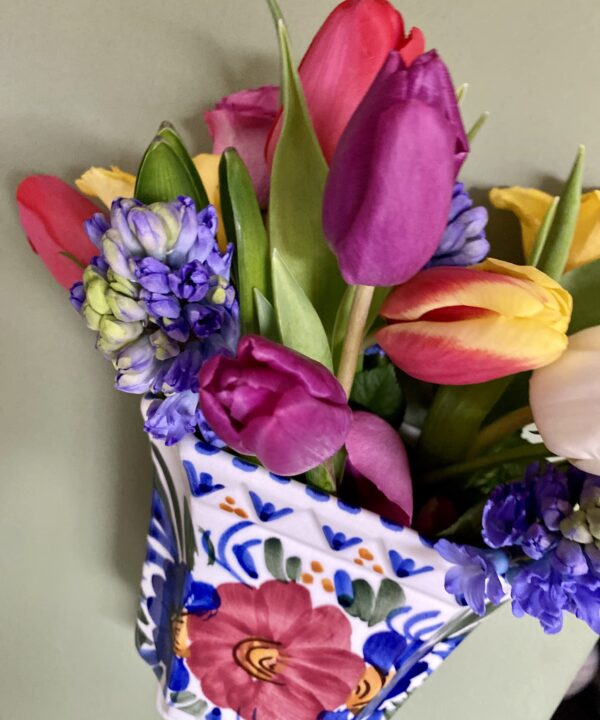 A vintage, wall-mounted vase filled with pretty tulips, hyacinths and roses.