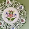 A hand-painted Portuguese wall plate with floral decoration hung against a green wall.