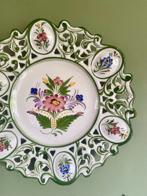A hand-painted Portuguese wall plate with floral decoration hung against a green wall.