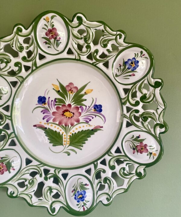 A hand-painted Portuguese wall plate with floral decoration hung against a green wall.