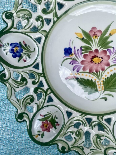 A glossy ceramic vintage wall plate from Portugal hand-painted with flowers.