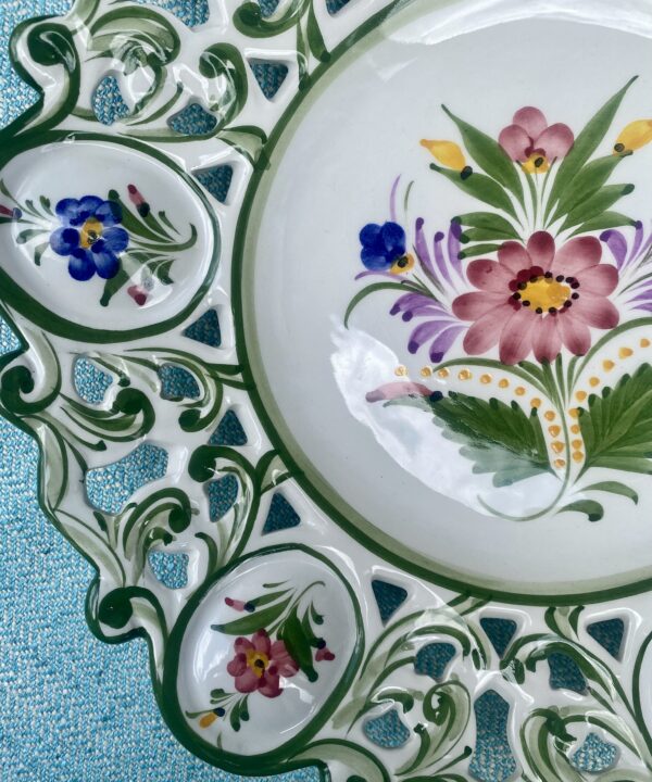 A glossy ceramic vintage wall plate from Portugal hand-painted with flowers.