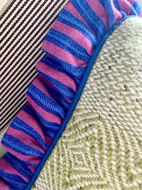 Irish linen frill on a green tweed cushion in pink and blue stripes.