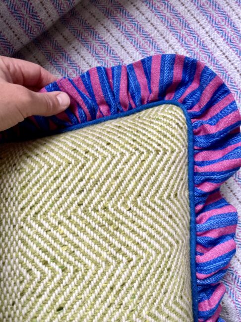 A handmade tweed cushion in lime green with a striped linen frill.