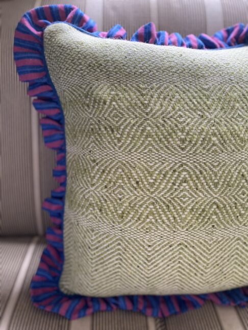 A Donegal tweed cushion in pale green with a blue and pink linen ruffled frill border.