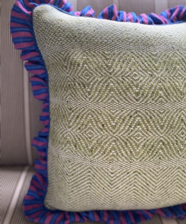 A Donegal tweed cushion in pale green with a blue and pink linen ruffled frill border.