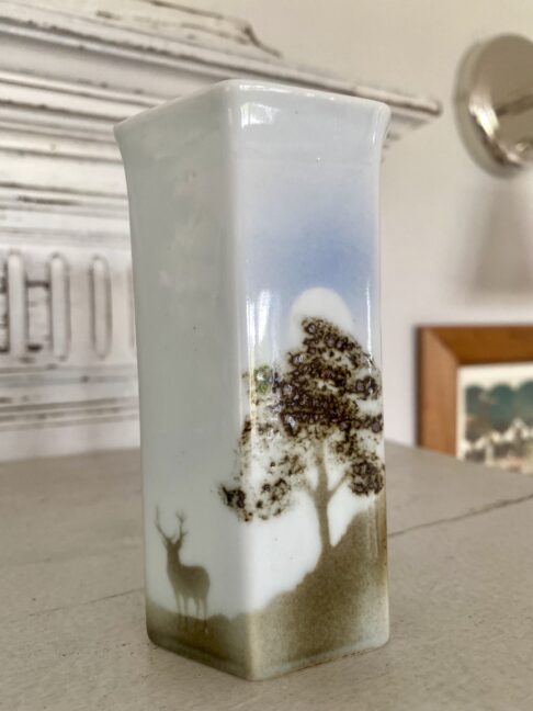 A stag and tree design on a pale grey and taupe brown porcelain bud vase.