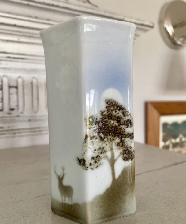 A stag and tree design on a pale grey and taupe brown porcelain bud vase.